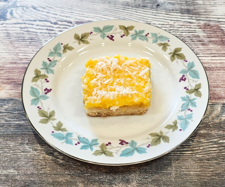 A piece of tropical papaya lemon bar on a round plate on a countertop.