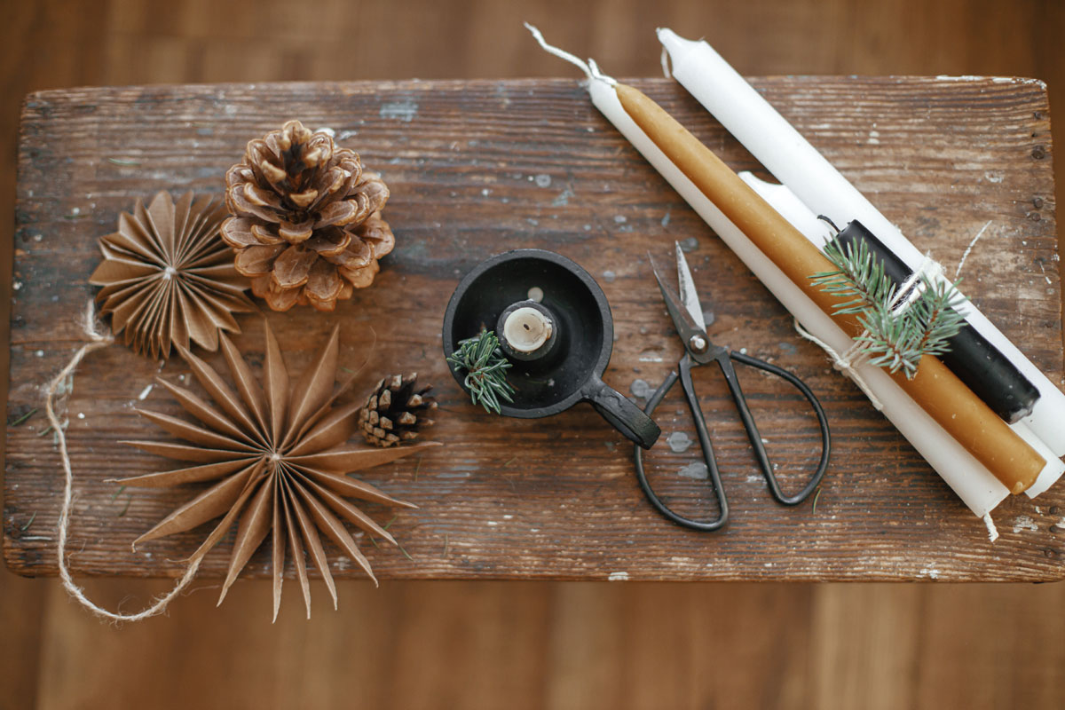 Nature craft items and beeswax candles, scissors on a board on a table.