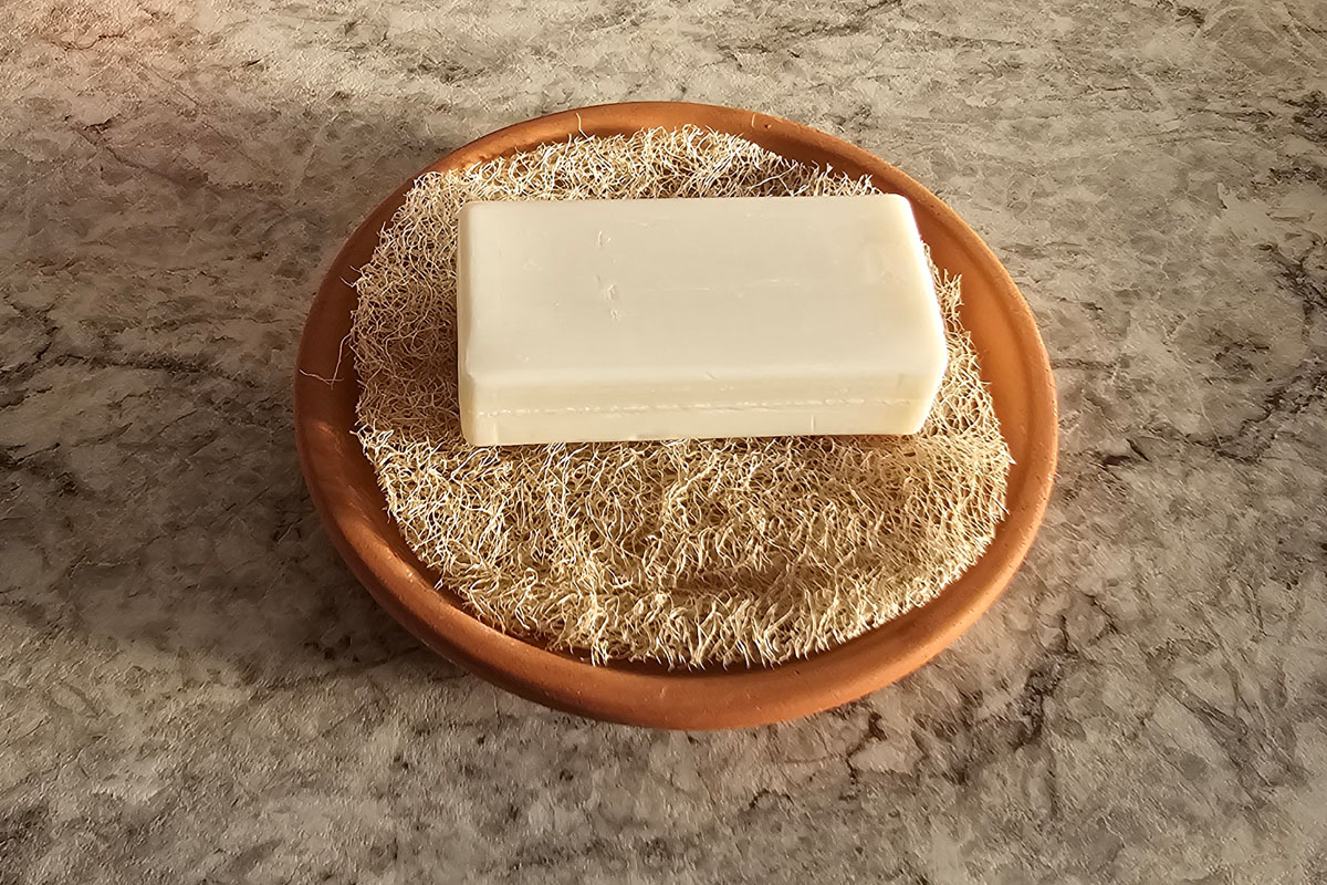 Soap dish riser crafted from a luffa gourd sponge sitting in a terracotta planter tray as a rustic styled soapdish.