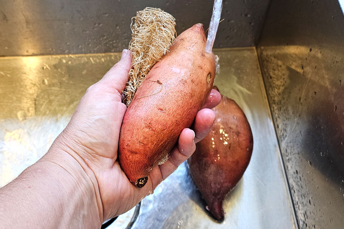 Scrubbing a sweet potato with a luffa gourd sponge.