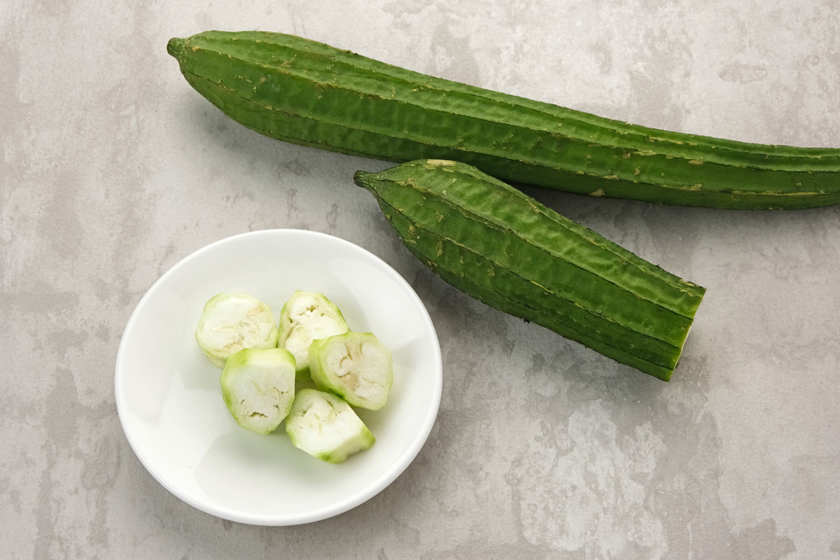 A whole angled luffa, and a partially sliced angled luffa on a tabletop.