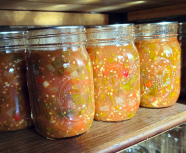 Photo pint jars of canned salsa sitting on a shelf in a canning cupboard.