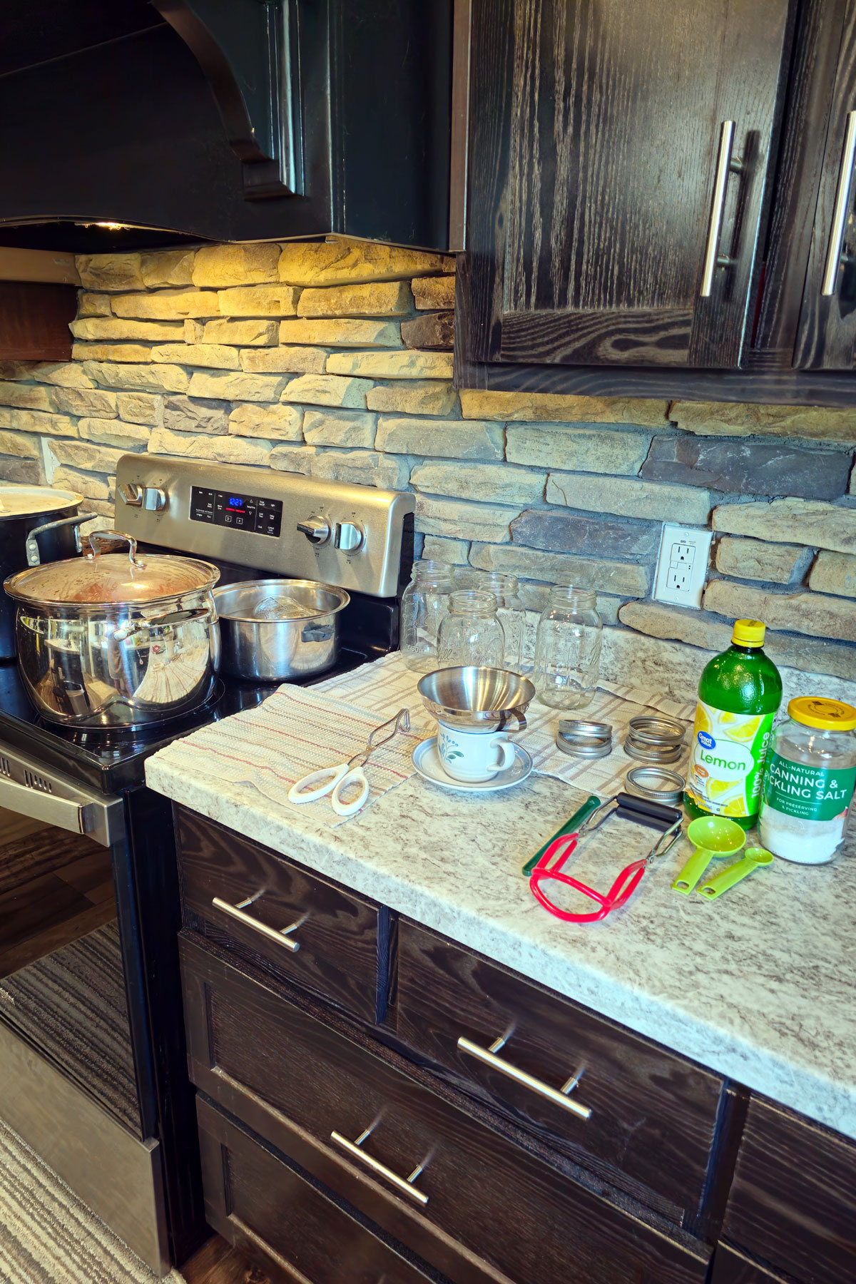 Canning setup by the stove with canning jars, lids, tools, lemon juice and salt.
