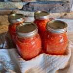 4 quart jars of home-canned tomatoes wrapped in kitchen towels on countertop.